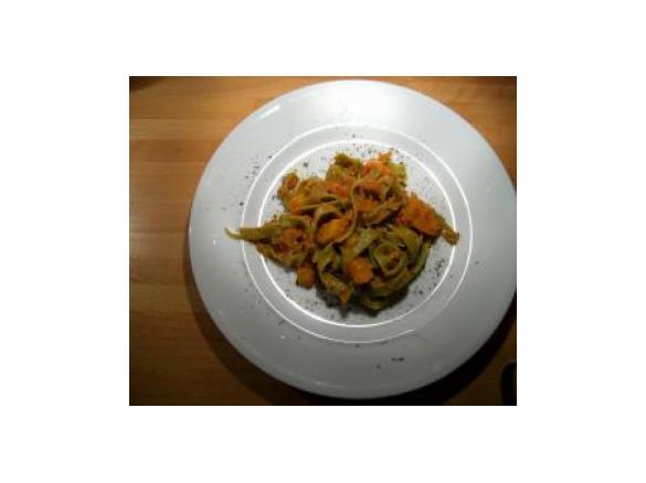 Grüne Bandnudeln mit Kürbiswürfeln in roter Soße